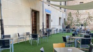 Un área de estar al aire libre con mesas y sillas, rodeada por un muro bajo y cubierta por una marquesina.