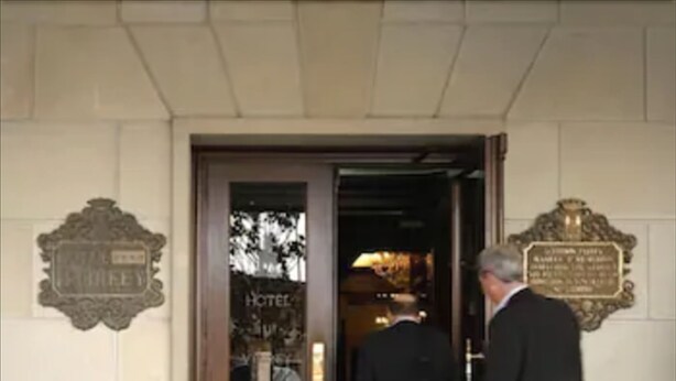Entrada de hotel con puerta de madera, un cartel sobre la puerta y una placa en la pared.