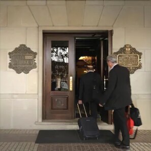 Entrada de hotel con puerta de madera, un cartel sobre la puerta y una placa en la pared.