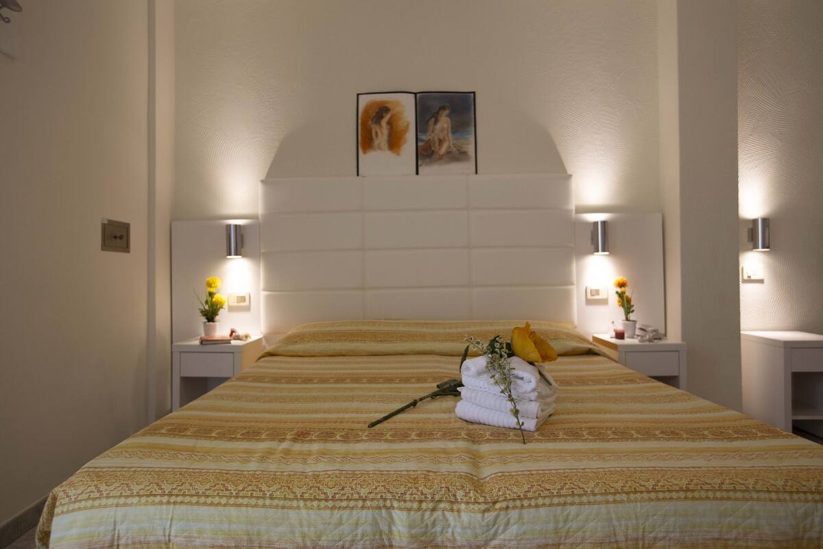 A neatly made bed with a patterned bedspread, two wall-mounted lamps, and a framed artwork above the headboard.