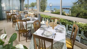 A dining area with tables set for four, overlooking a scenic view of the sea and a pier. - Hotel Gloria (Gabicce Mare)