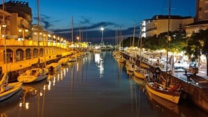 A marina at dusk with boats docked along the water, buildings on either side, and street lamps illuminating the area. - Hotel Gloria (Gabicce Mare)