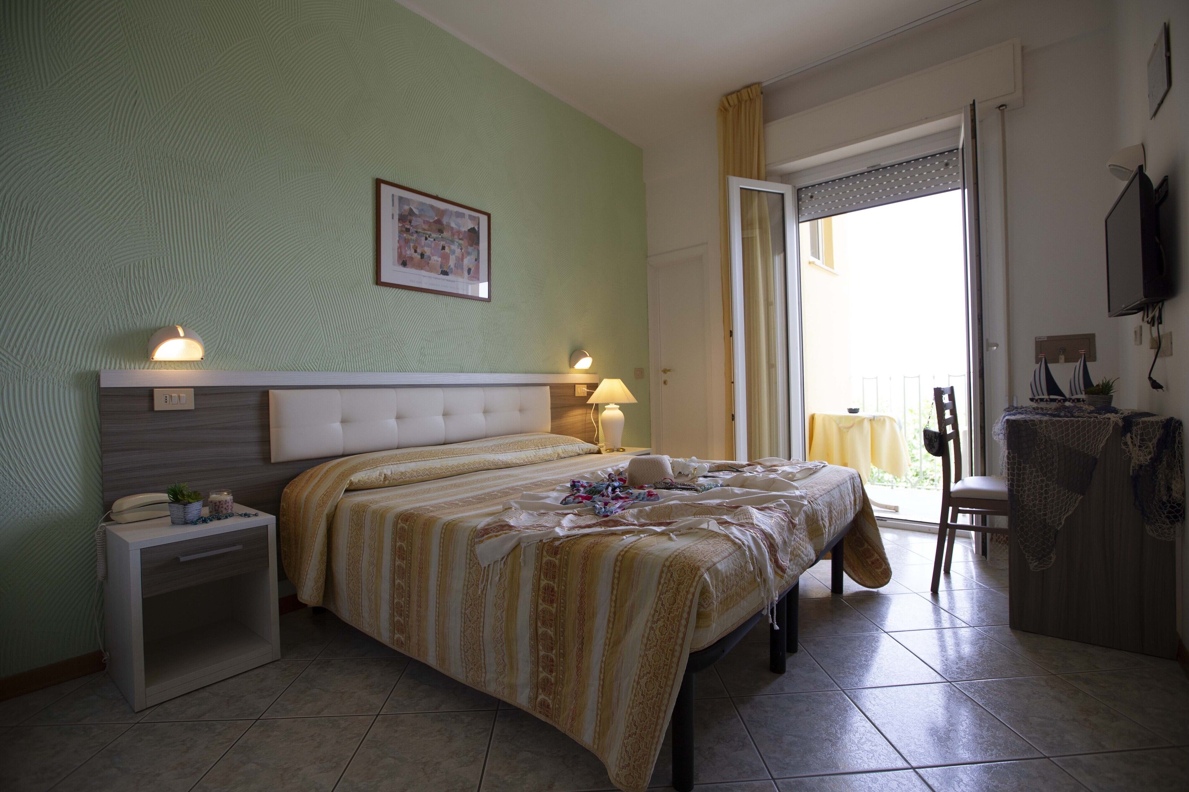 A hotel room with a bed, bedside tables, a chair, a desk, and a view through a door.