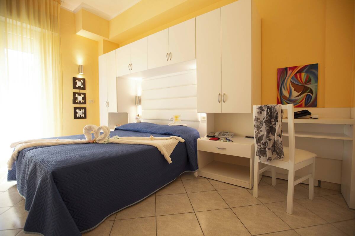 A bedroom with a bed, a desk, a chair, and a painting on the wall.