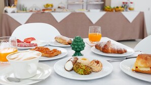 Een ontbijtbuffet met diverse gebakjes, een koffiekop en een glas sinaasappelsap.