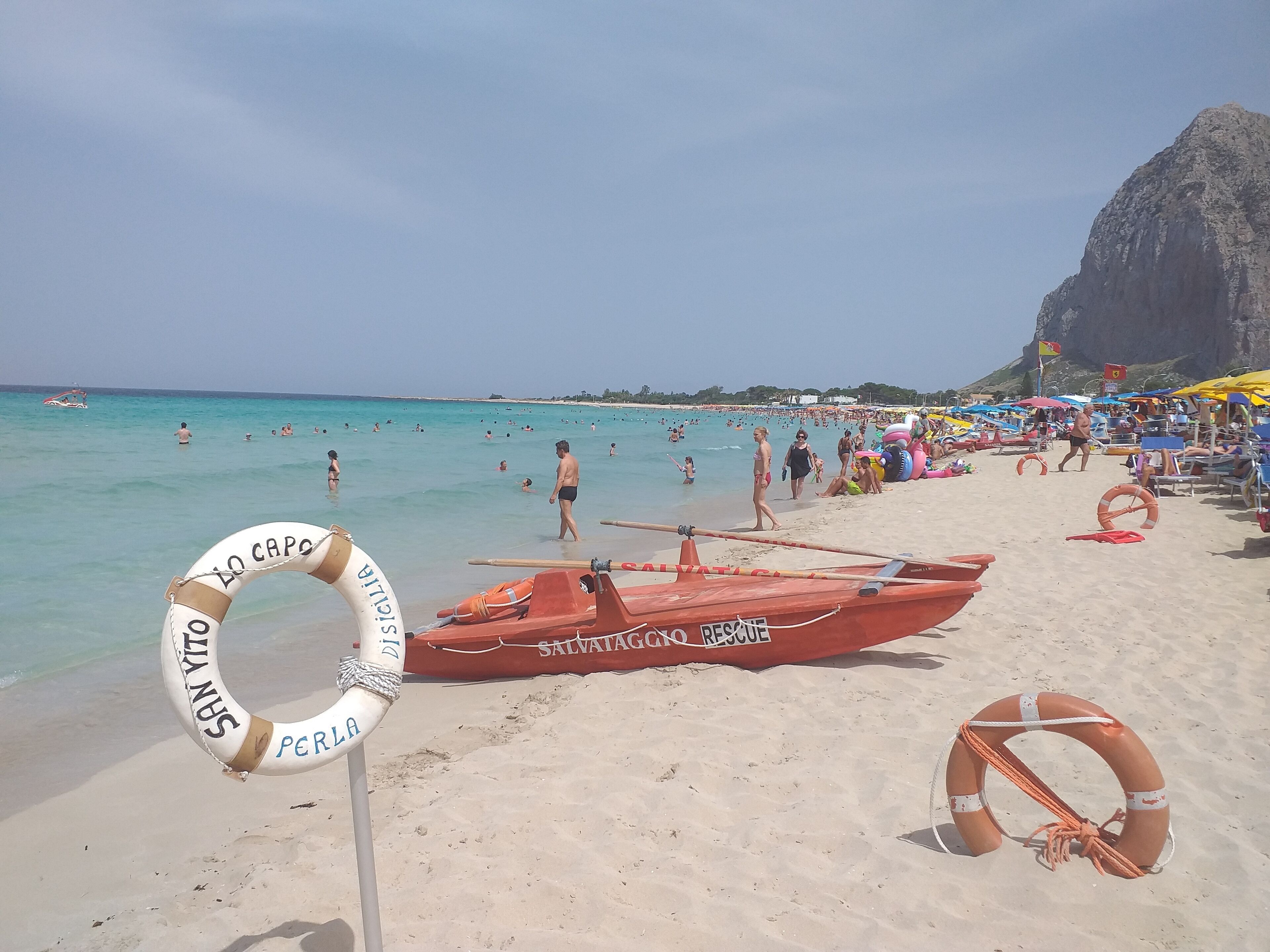 A beach with lifebuoys, a rescue boat, and people swimming.