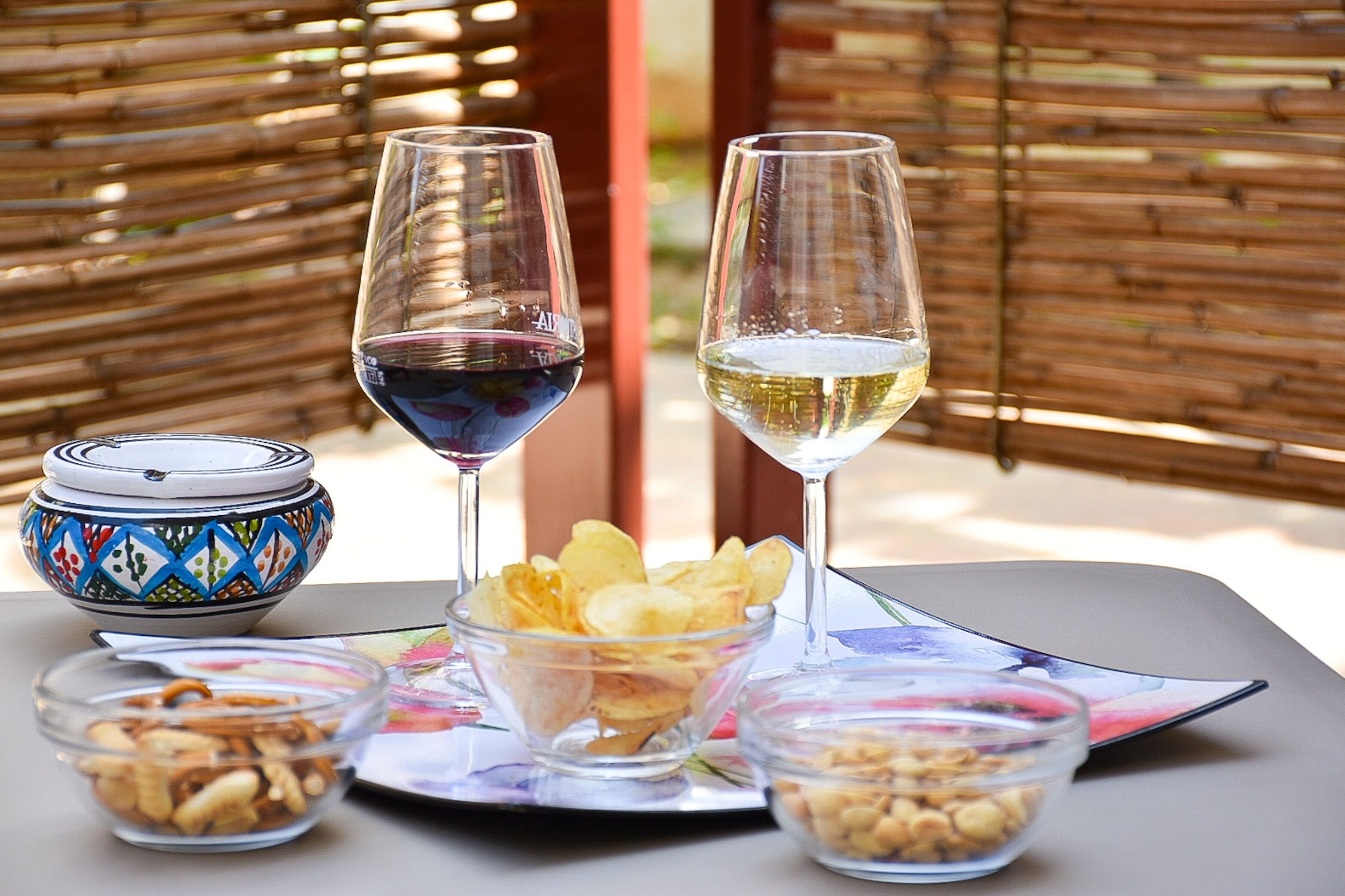 A table with two wine glasses, a bowl of chips, and two small bowls of nuts.