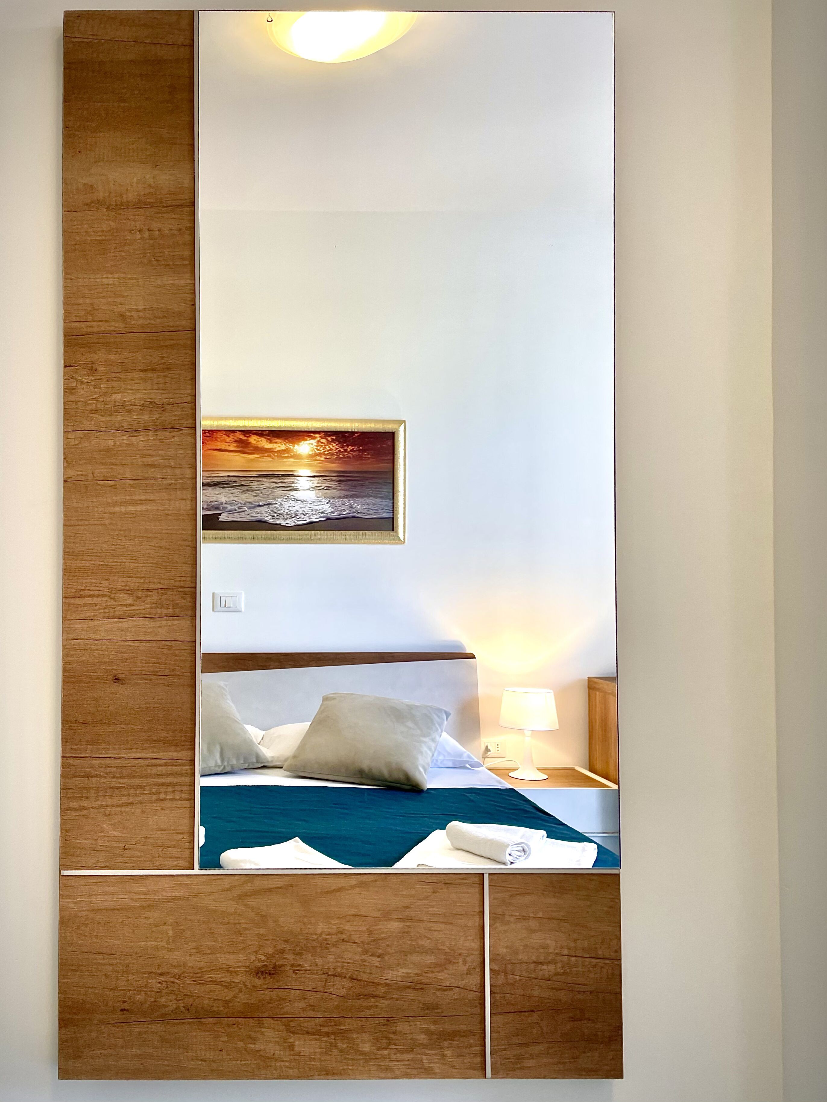 Une chambre d’hôtel avec un lit, une table de chevet, une lampe et un tableau représentant un coucher de soleil sur l’océan.