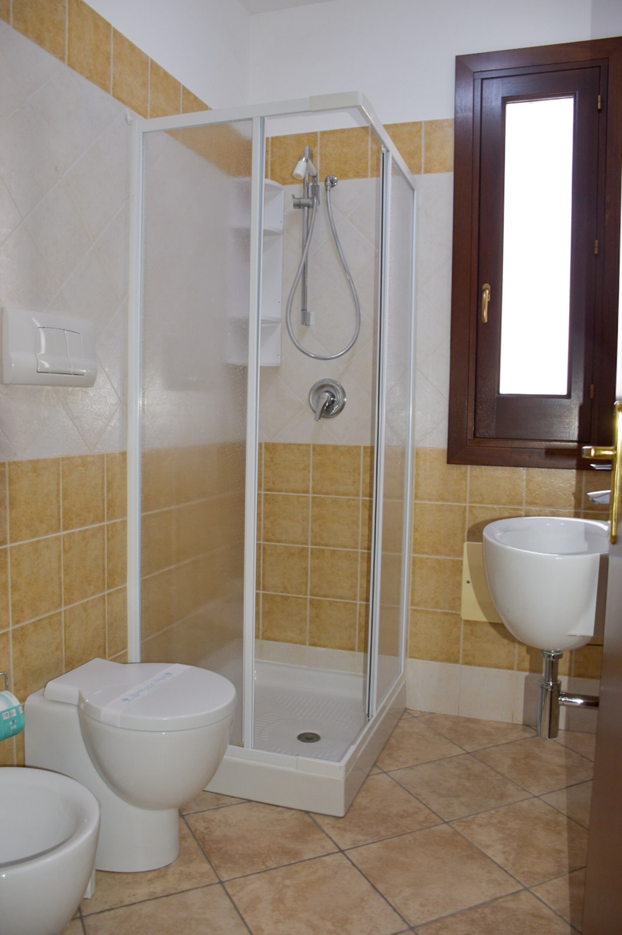 A bathroom with a glass-enclosed shower, a white sink, and two toilets.
