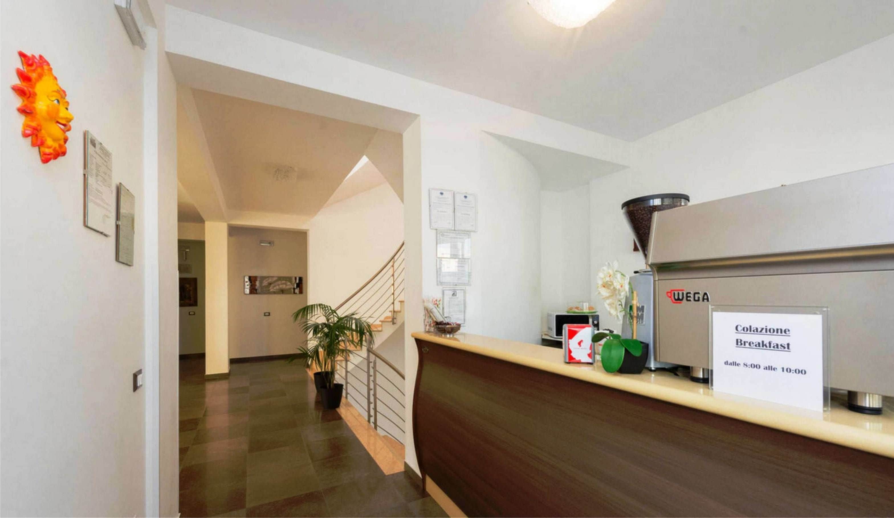 Een hotel receptie met een koffieapparaat met de aanduiding 'WEGA' en een bord waarop de ontbijttijden staan.
