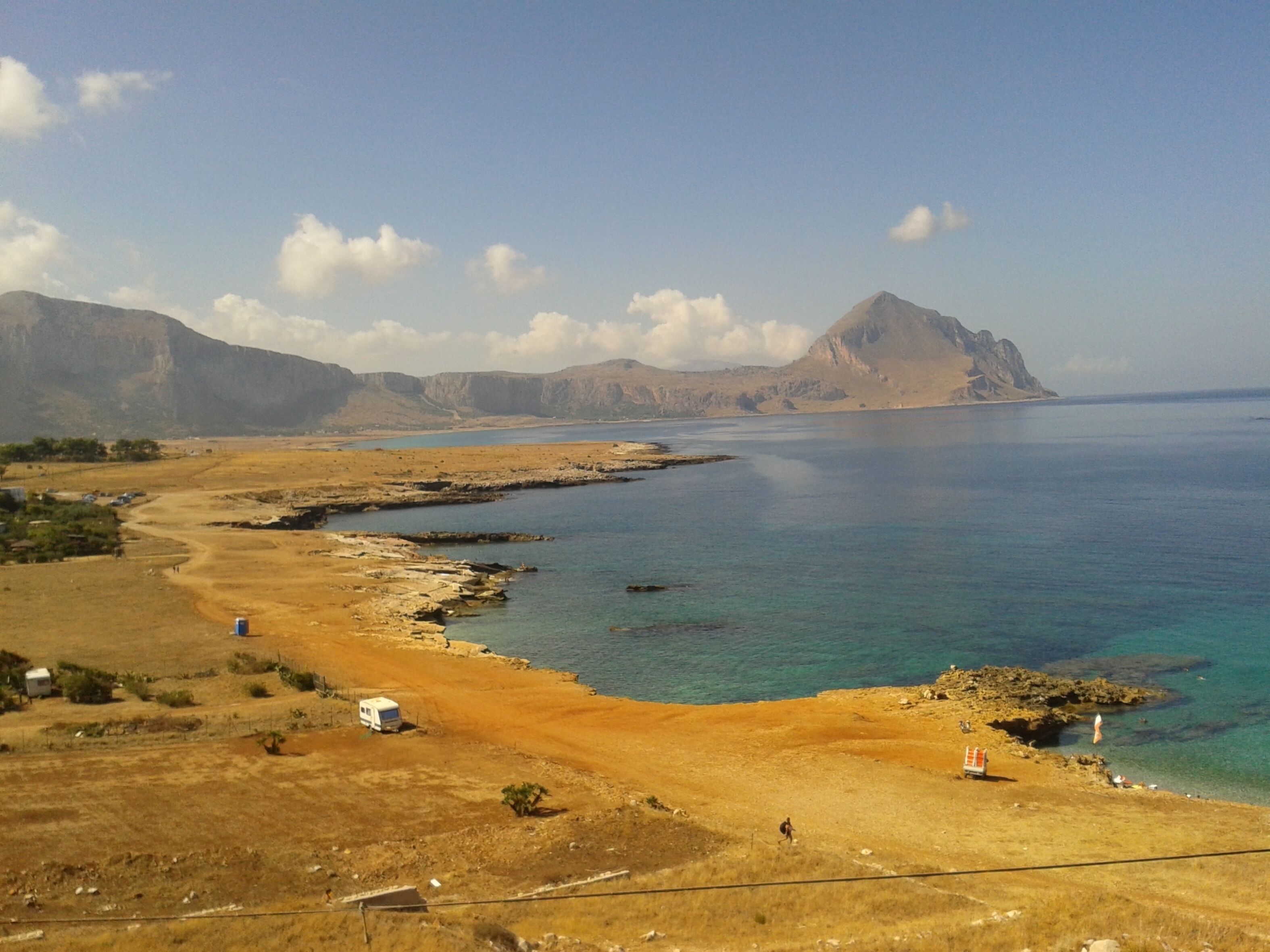 Un paysage côtier offrant une vue dégagée sur la mer, une plage de sable et des montagnes lointaines.