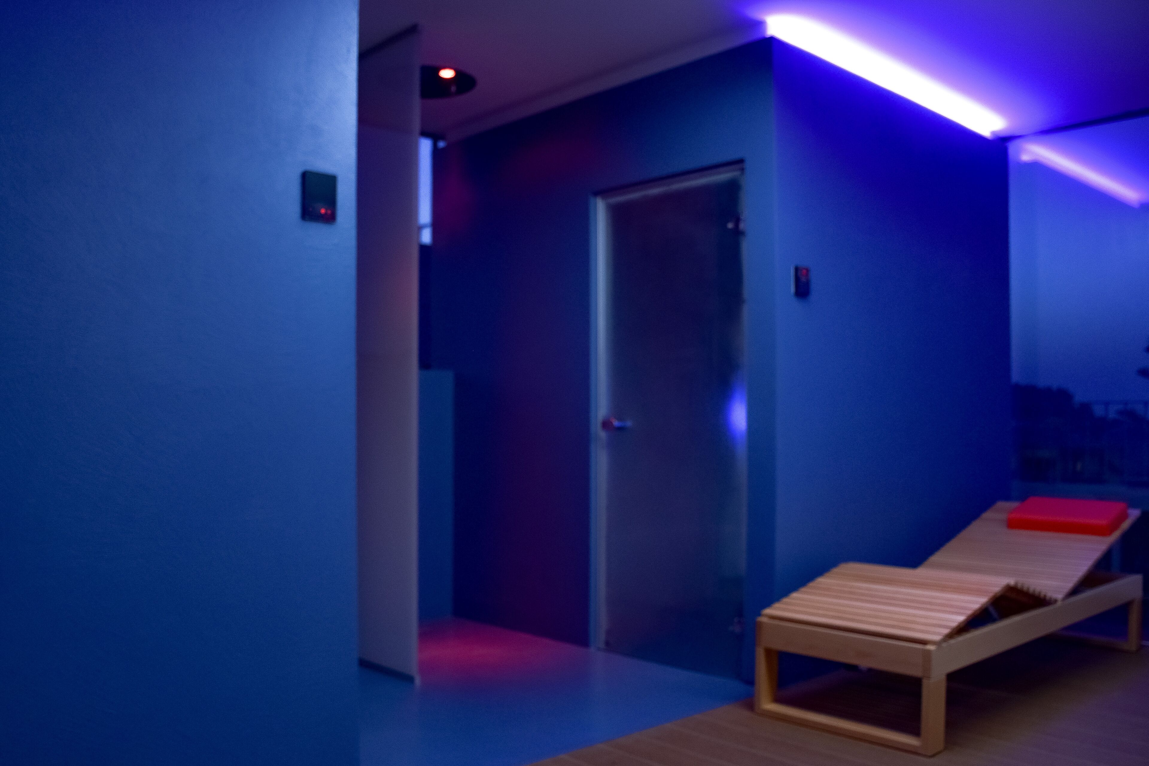 A room with a wooden bench, a door, and blue lighting.