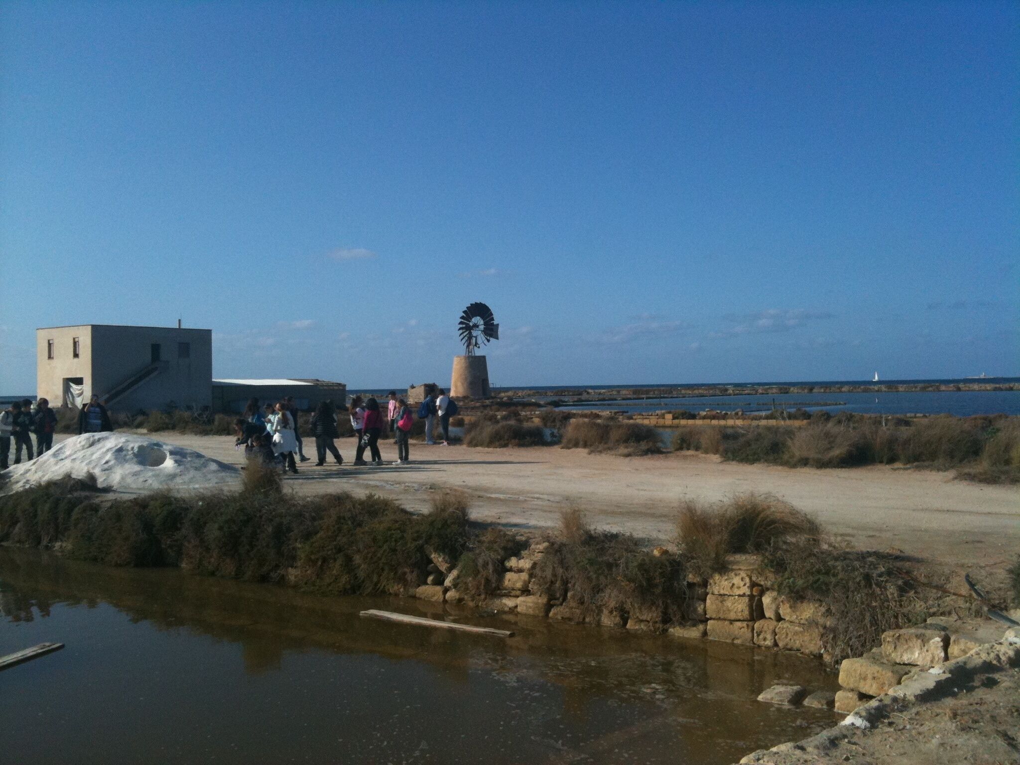 Una zona costera con un molino, un edificio y un grupo de personas.