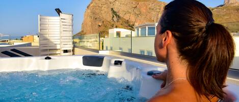 A person relaxing in a hot tub with a mountainous backdrop.