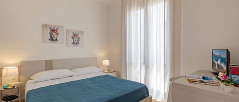 A hotel room with a bed, bedside tables, a desk, and a TV.