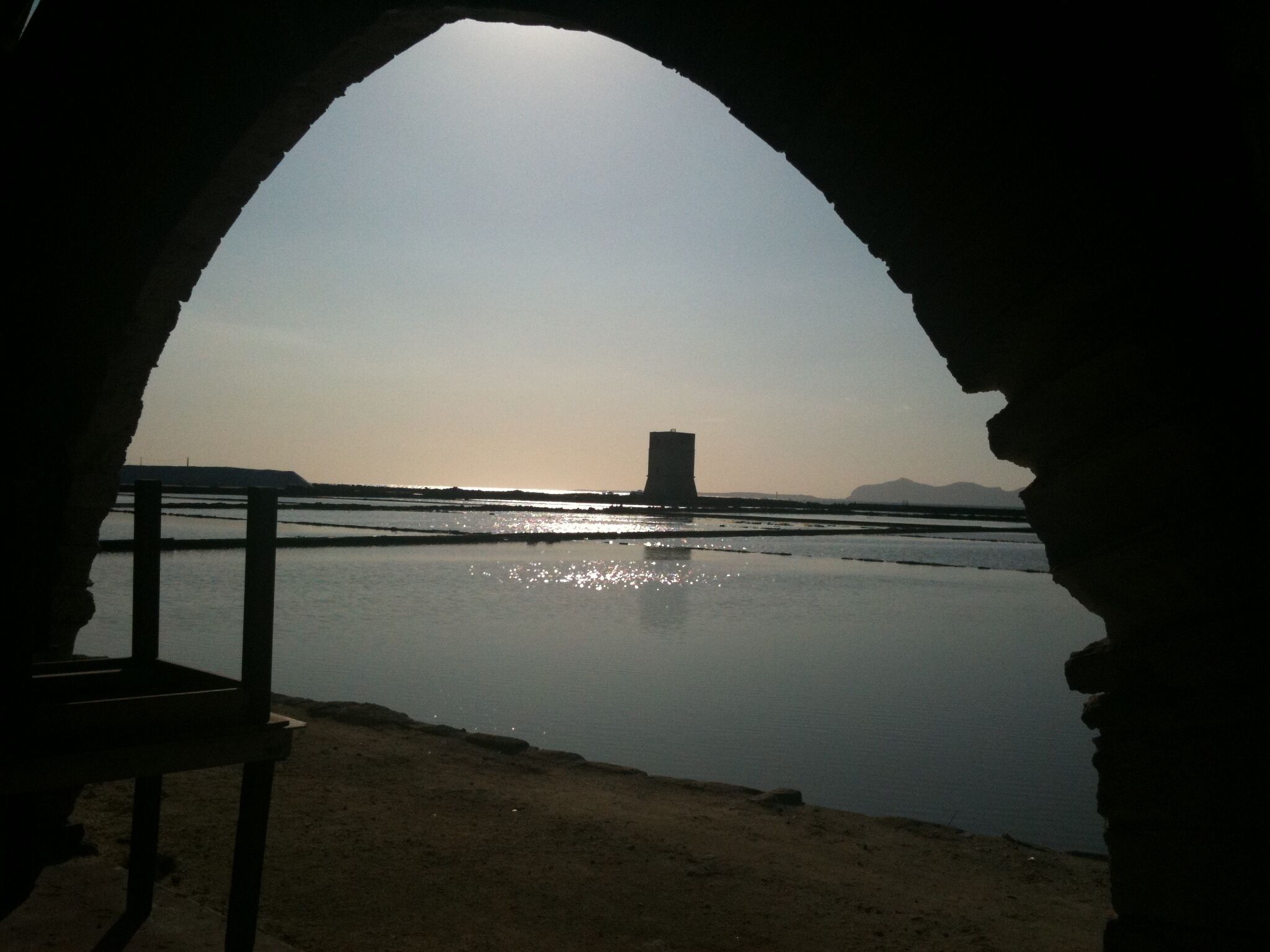 A view through an arched doorway overlooking a calm body of water with a distant structure.