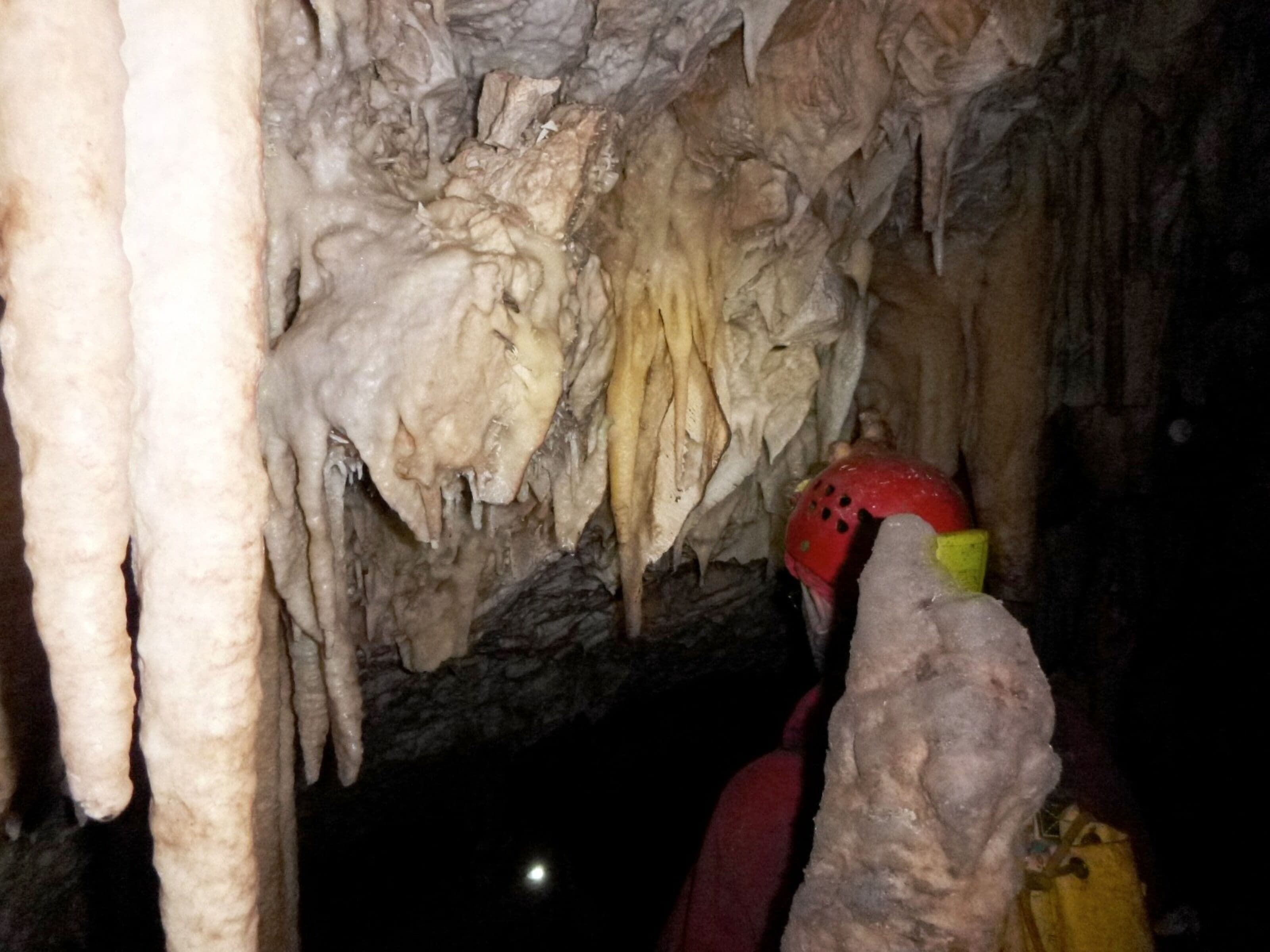 Eine Höhle mit Stalaktiten und Stalagmiten, eine Person mit Helm und Taschenlampe.