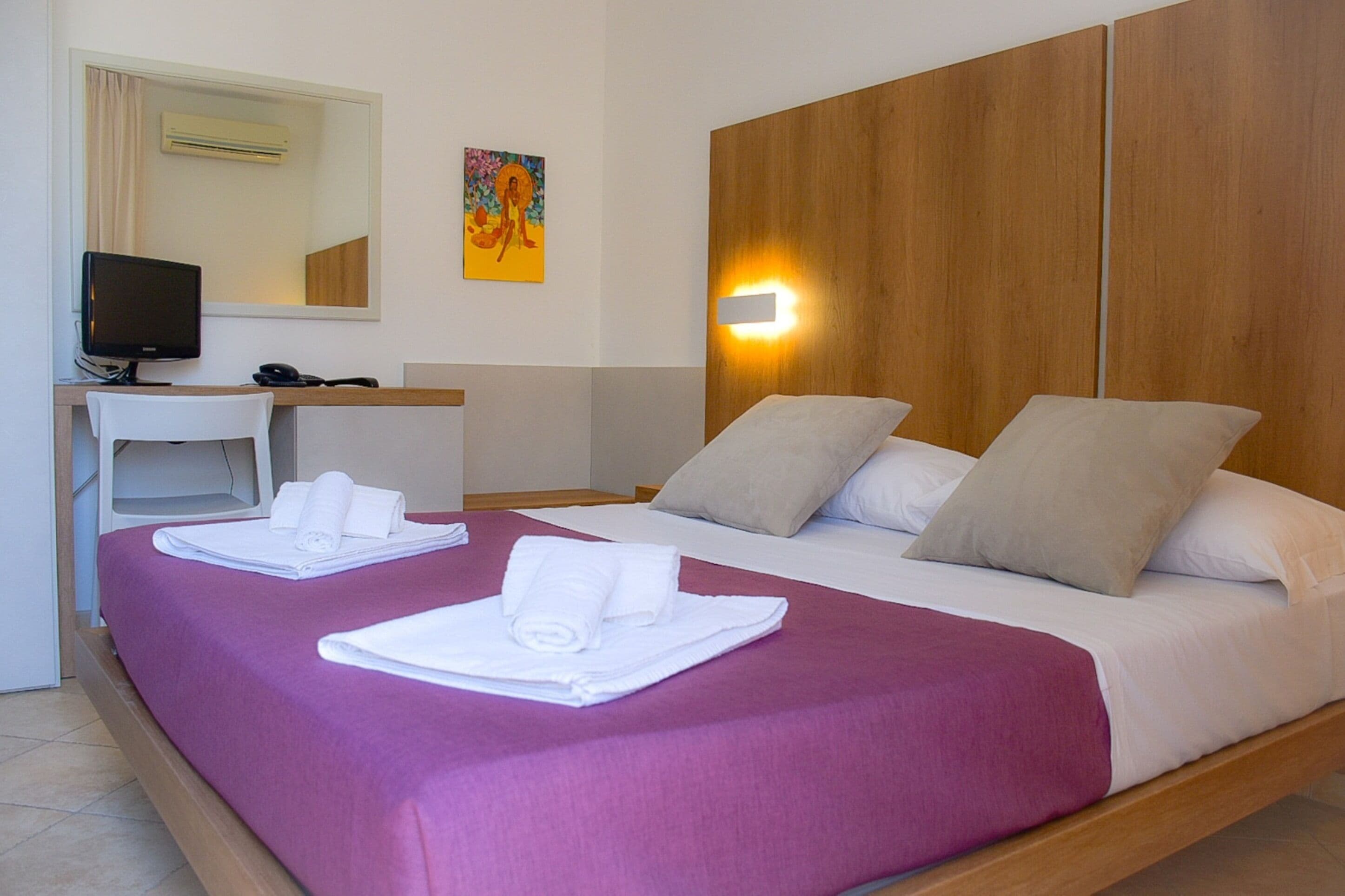 Ein Hotelzimmer mit zwei Betten, einem Schreibtisch, einem Fernseher und einem Bild an der Wand.