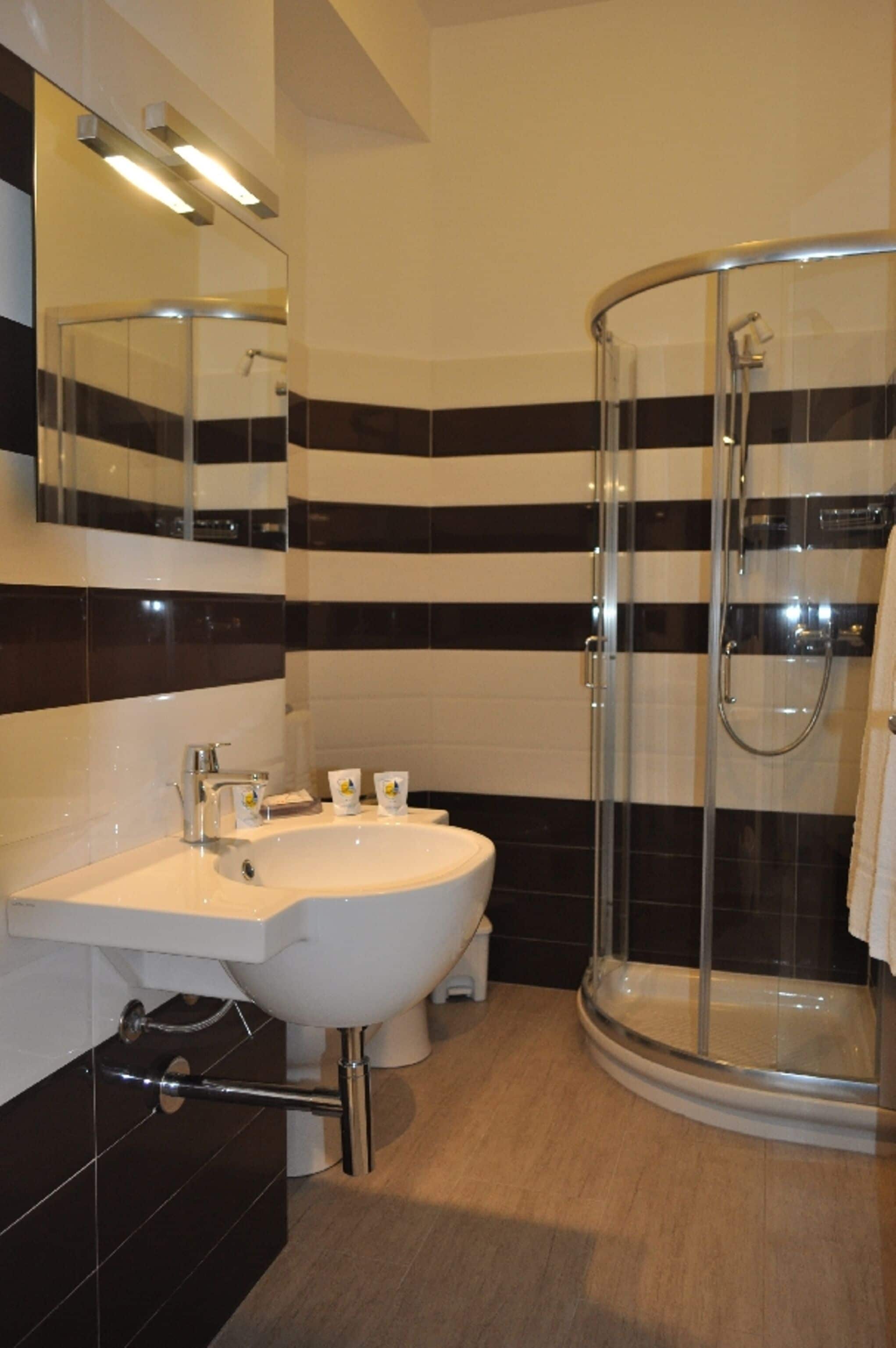A bathroom with a white sink, a glass-enclosed shower, and black and white striped tiles.