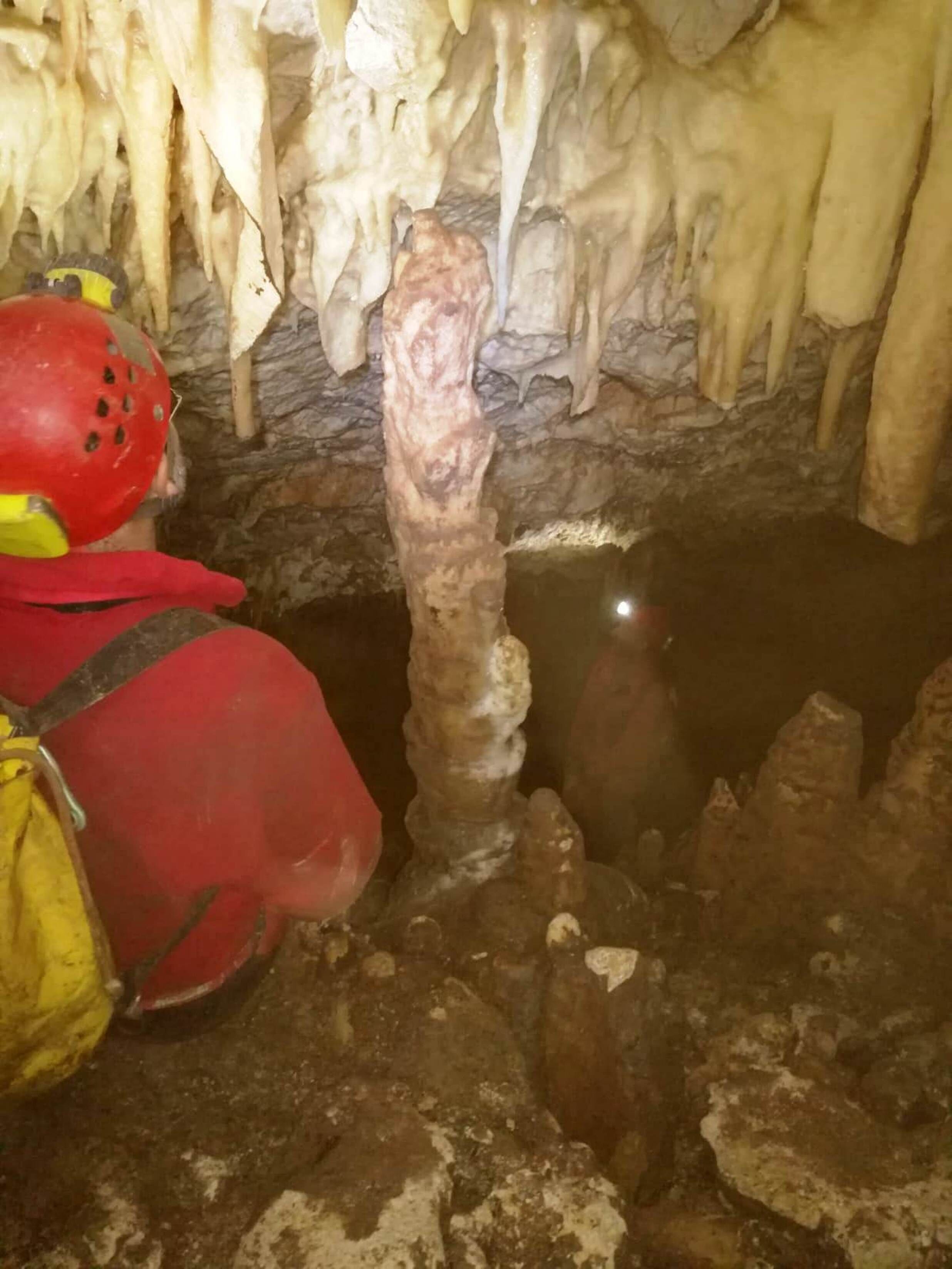 A cave interior with stalactites and stalagmites, a red helmet, and a yellow bag.
