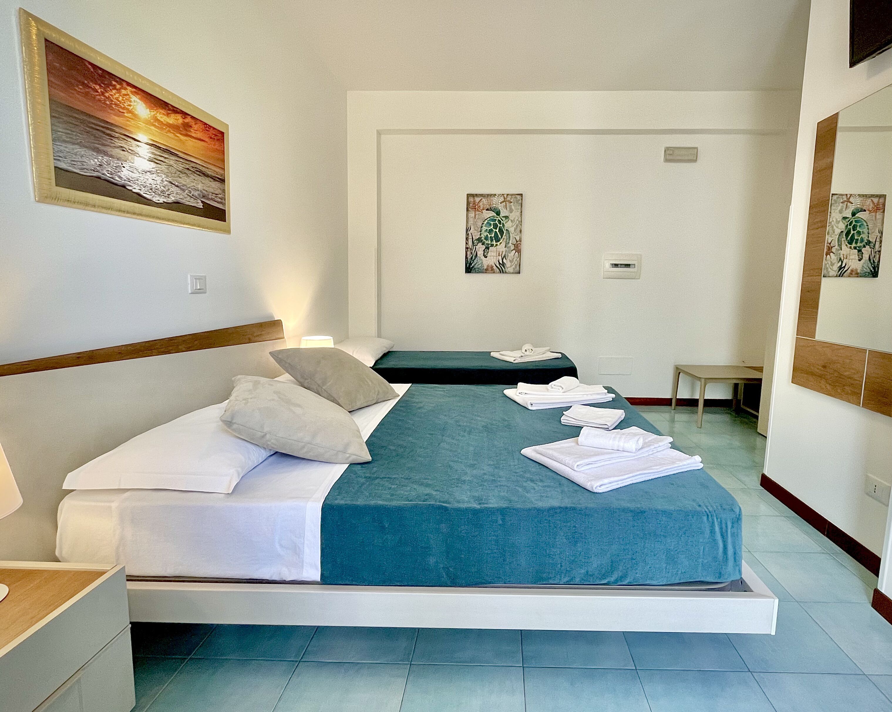 Een hotelkamer met een bed, kussens, een nachtkastje, een stoel en kunst aan de muren.