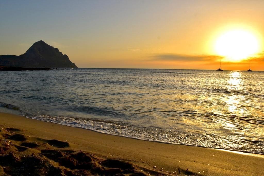 A beach with a mountain in the background and the sun setting over the water.