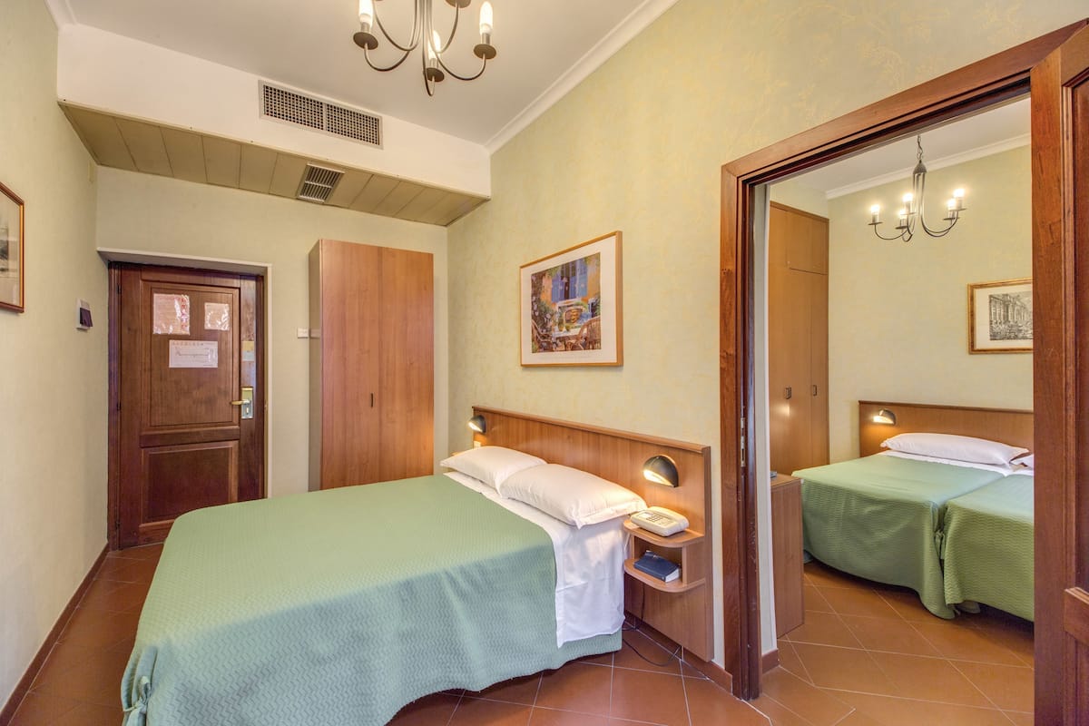 A hotel room with two beds, a wooden wardrobe, a bedside table with a lamp, and a mirror.