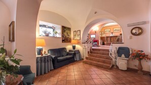 A spacious living area with a sofa, a coffee table, and a lamp. There is a staircase leading to an upper floor. - Hotel Corona (Rome)