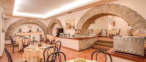 A dining area with brick arches, tables set with white tablecloths, and a central island with a coffee machine.