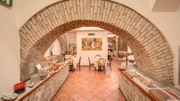 An indoor dining area with brick arches, a buffet with various food items, and a painting on the wall. - Hotel Corona (Rome)