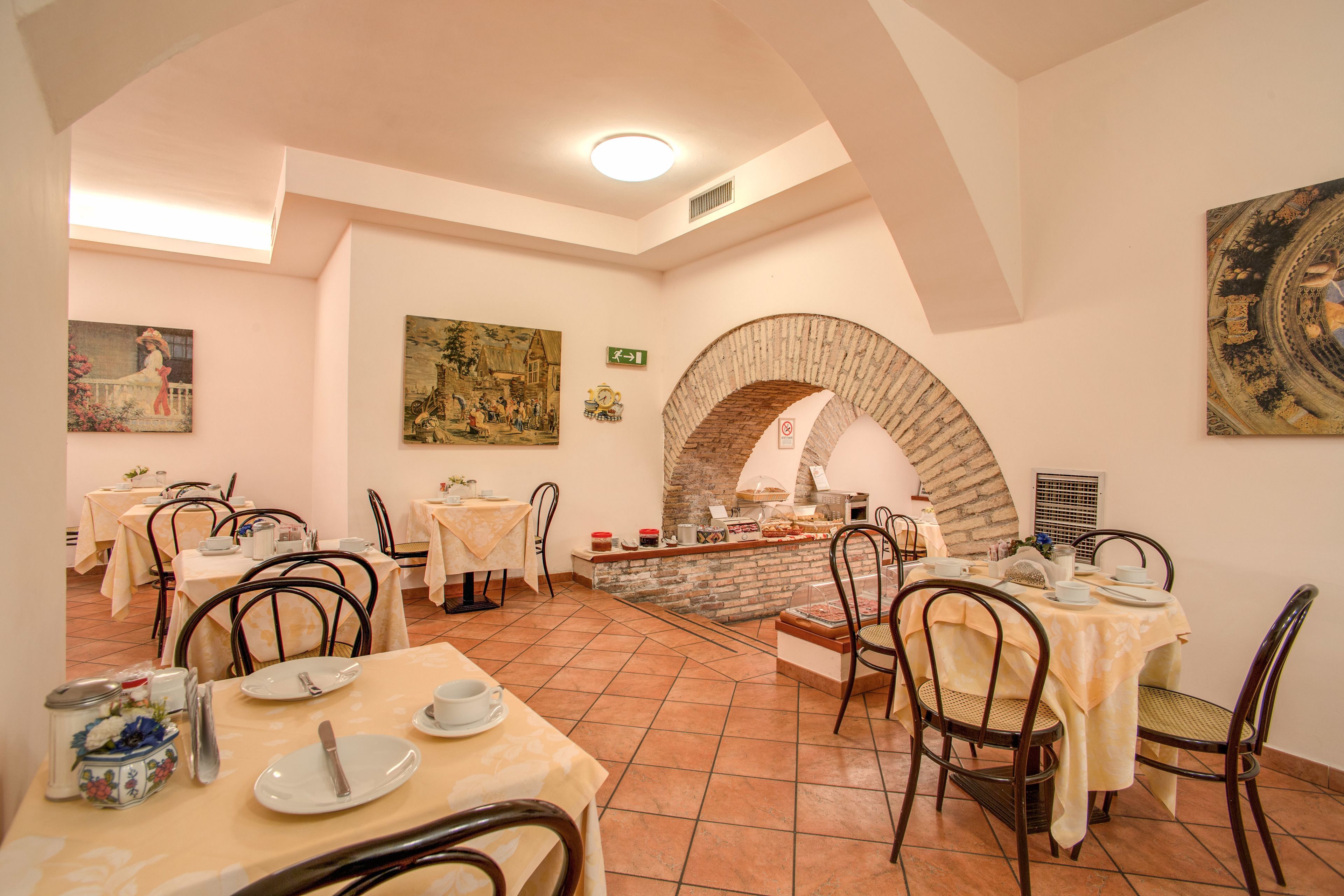 A dining area with multiple tables and chairs, a brick archway, and artwork on the walls.