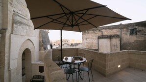 A terrace with a table and chairs, a large umbrella, and a stone wall. - Albergo del Sedile (Matera)