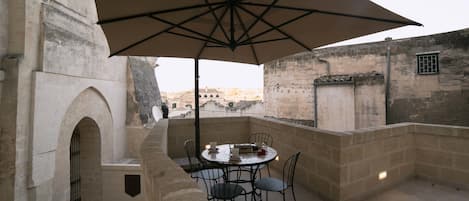 Une terrasse avec une table et des chaises, un grand parasol et un mur en pierre.
