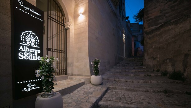 An outdoor pathway leading to a building with a large illuminated sign for 'Albergode del Sedil'. - Albergo del Sedile (Matera)