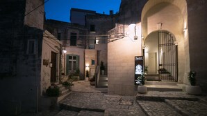 A stone courtyard with a central archway, potted plants, and a sign indicating a hotel entrance. - Albergo del Sedile (Matera)