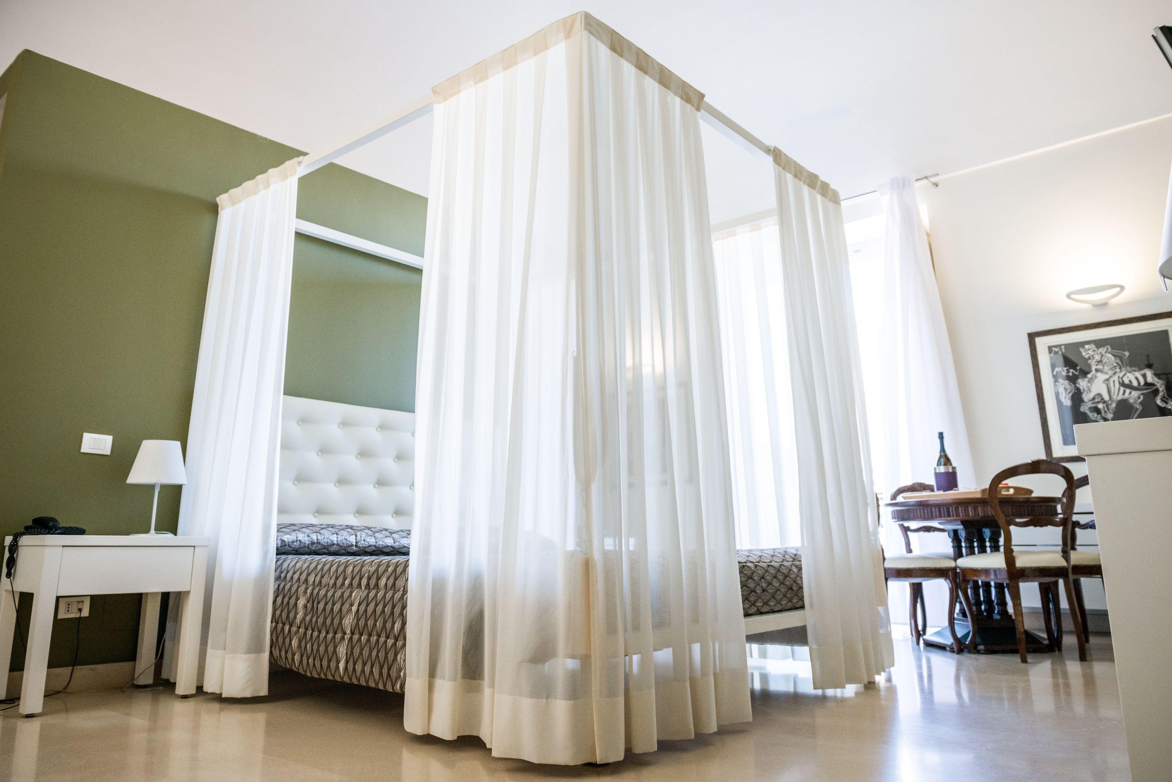 A bedroom with a four-poster bed, a bedside table with a lamp, and a chair.