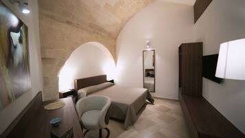 A bedroom with a bed, a chair, a desk, a mirror, and a TV.