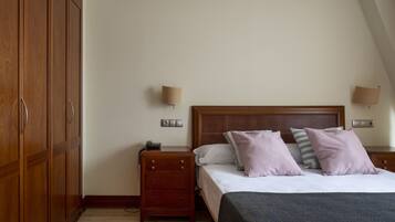 Un dormitorio con un armario de madera, una mesita de noche con lámpara, una cama con almohadas y un atril.