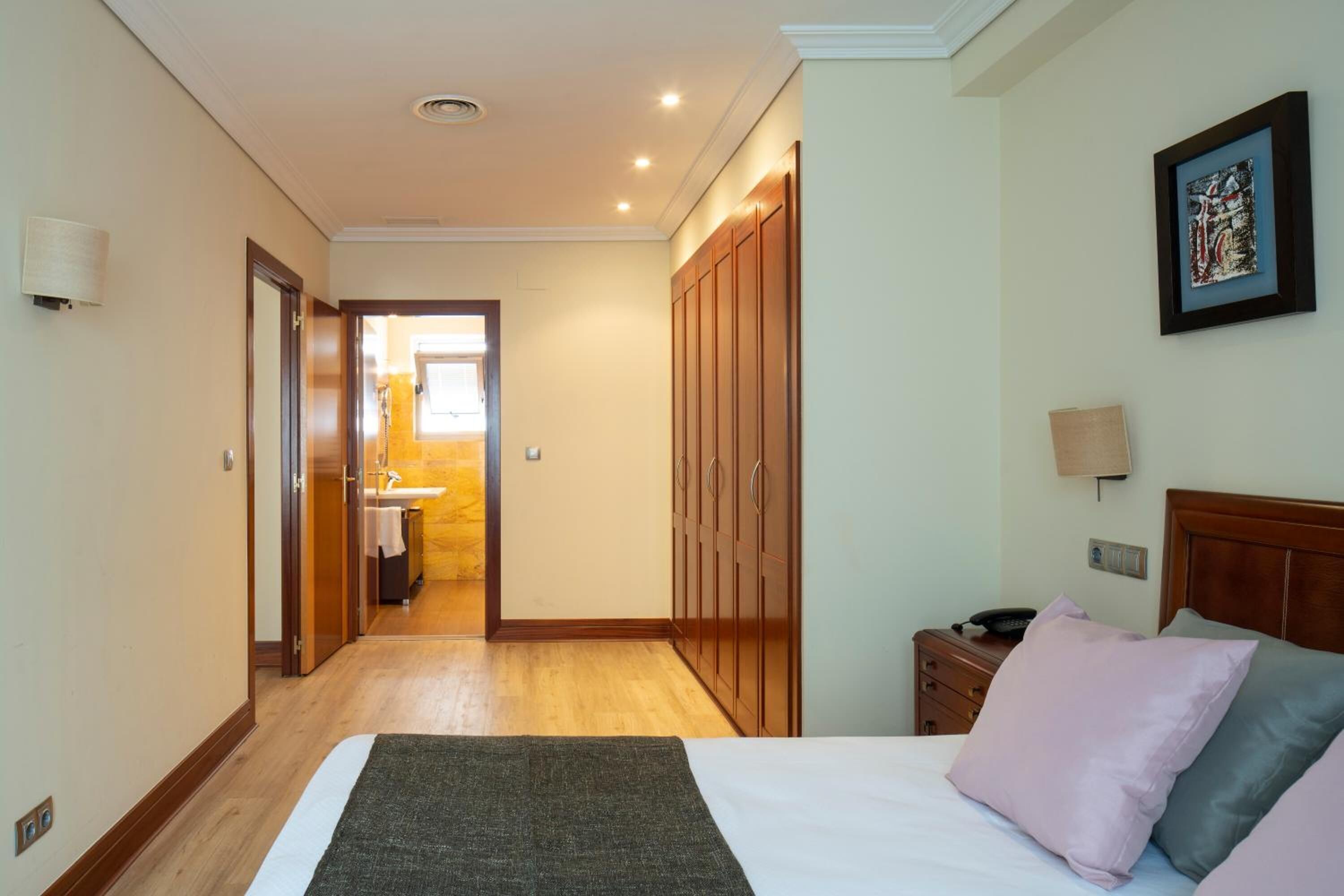 Una habitación de hotel con cama, mesita de noche, lámpara, armario y vistas al baño.