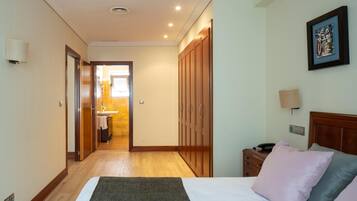 Una habitación de hotel con cama, mesita de noche, lámpara, armario y vistas al baño.