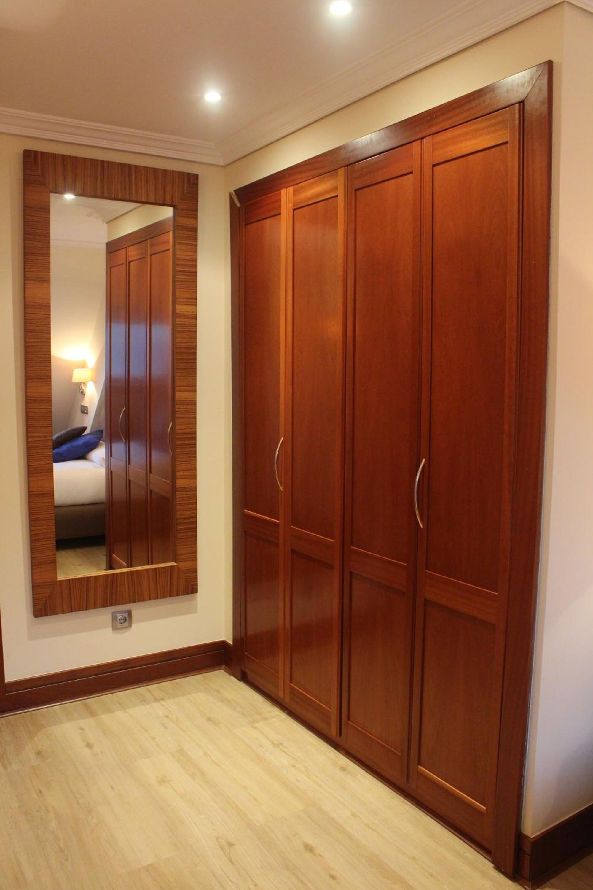 Un armario de madera con espejo, una cama con almohada azul y una lámpara de noche en una habitación de hotel.