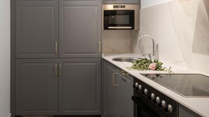 Une cuisine moderne avec des armoires grises, un four encastré, un évier en acier inoxydable et un plan de travail en marbre.
