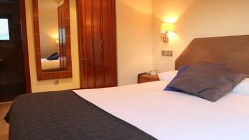 A hotel room with a large bed, wooden wardrobe, a mirror, and a wall-mounted lamp.