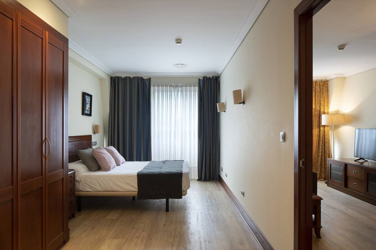 A hotel room with a bed, wooden wardrobe, bedside table, lamp, and curtains.