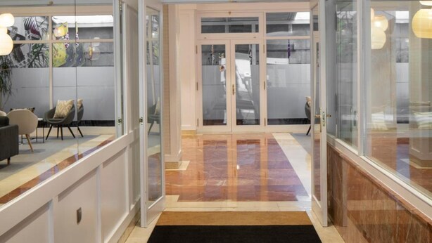 Un hall d’hôtel moderne avec une cloison en verre, un tapis noir et marron et un luminaire au plafond.