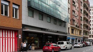 Un bâtiment moderne à la façade de verre, situé à côté d’un bâtiment en briques surmonté d’un auvent rayé de rouge et de blanc.