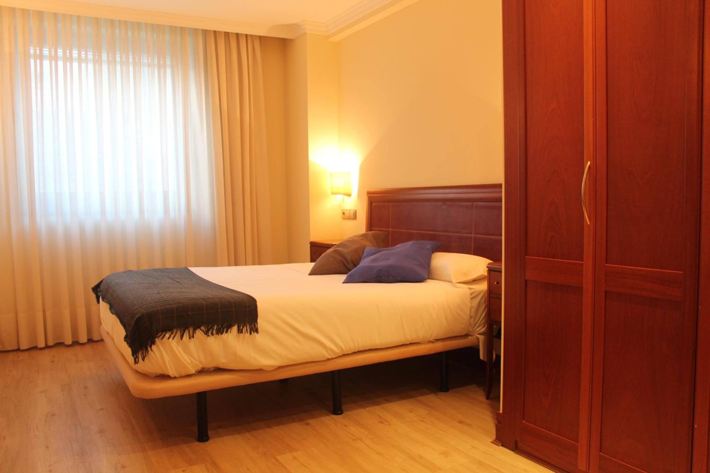 Una habitación de hotel con cama, mesita de noche, lámpara y armario.