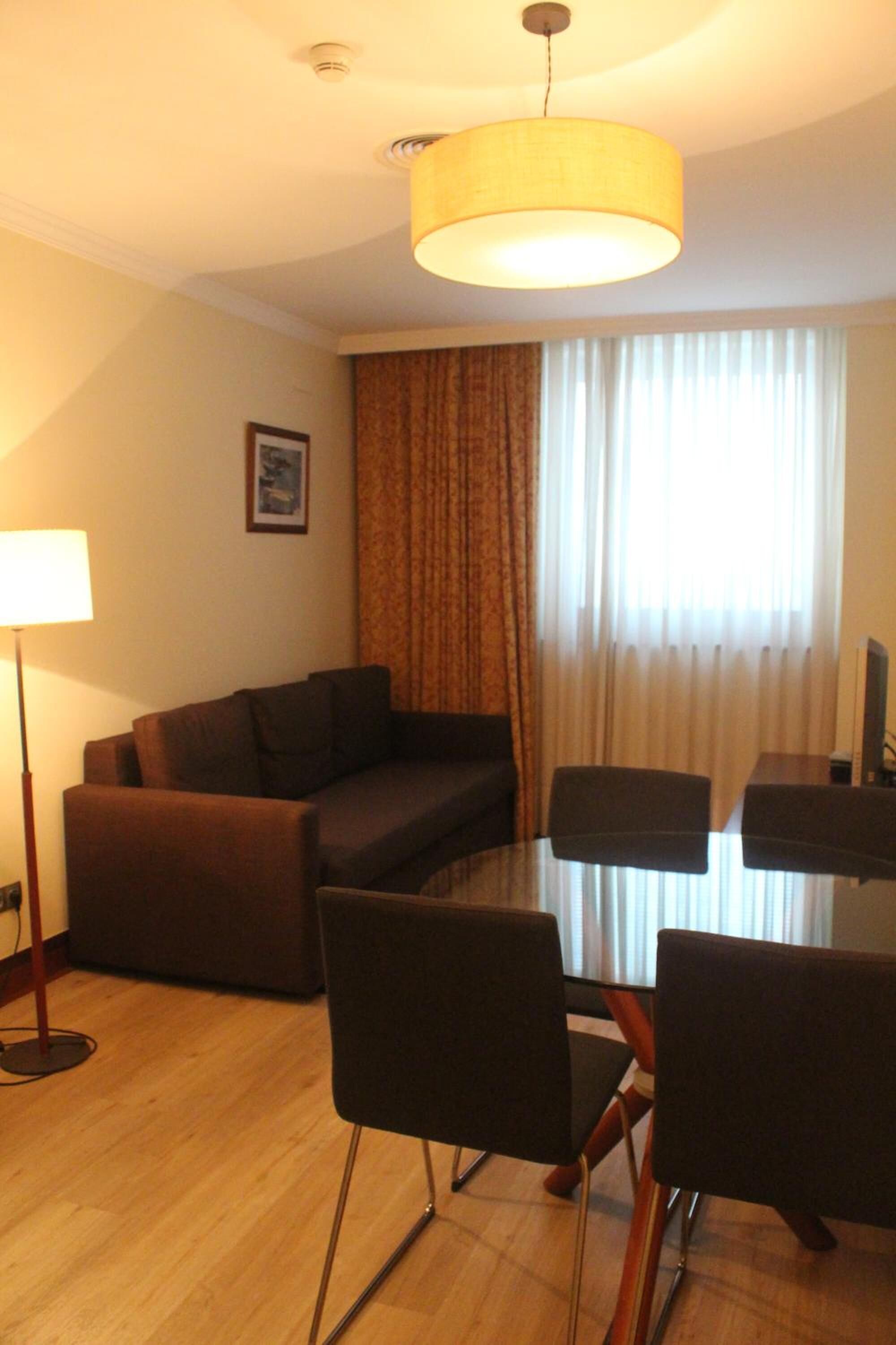 Una sala de estar moderna con un sofá, una mesa de comedor con superficie de vidrio y sillas.