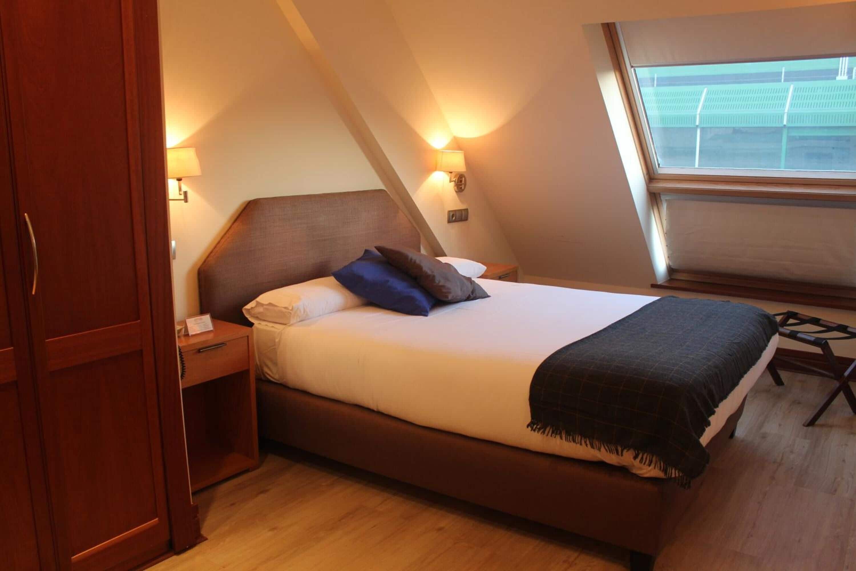Un dormitorio con cama, mesitas de noche y ventana con vista a un edificio.