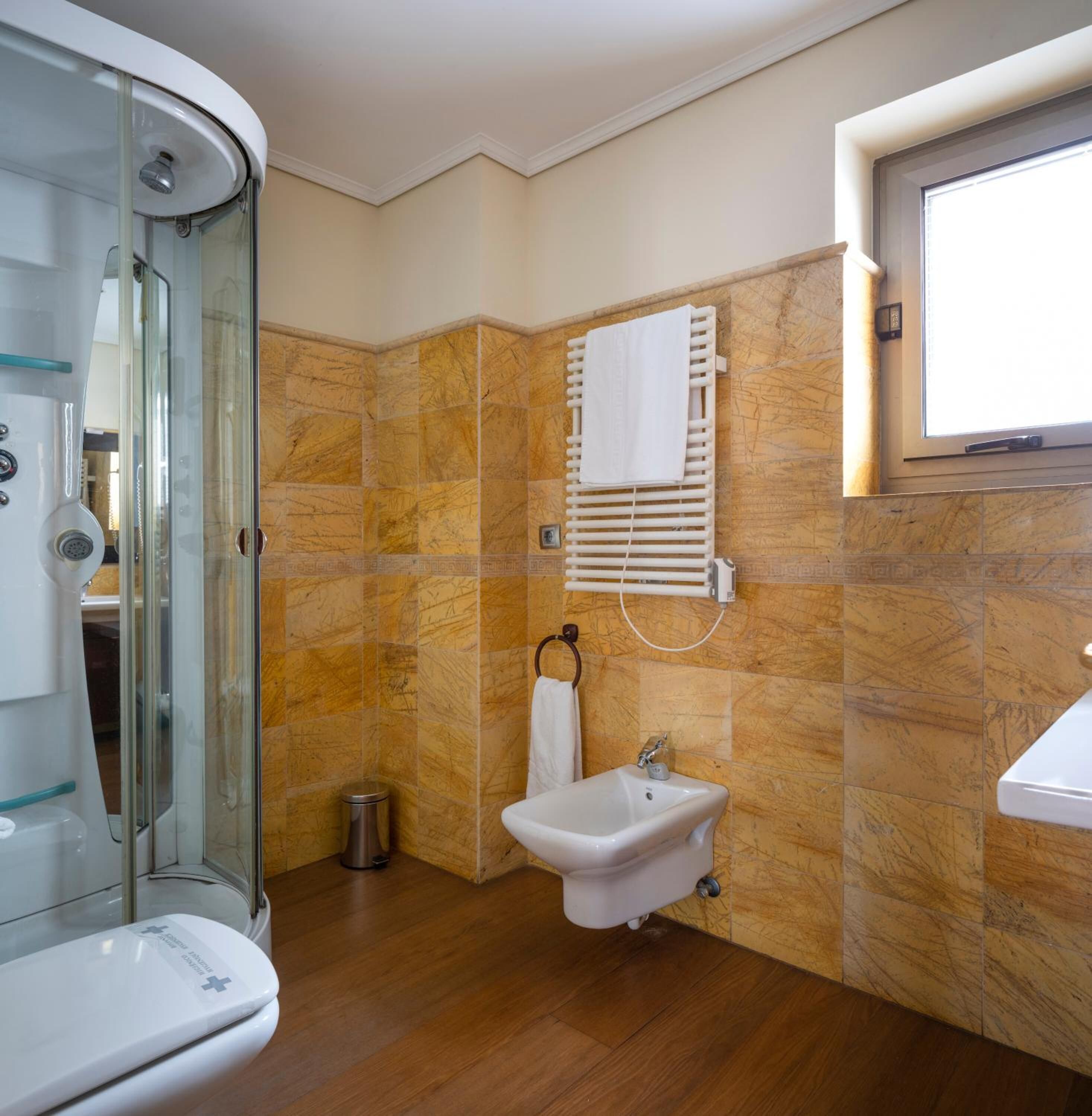 Un baño con cabina de ducha de vidrio, un lavamanos blanco y un perchero para toallas.